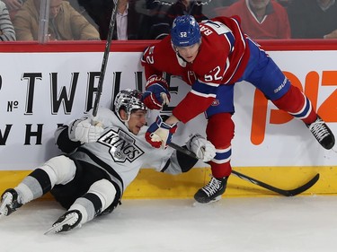 A Kings player lis on the ice at the boards underneath a Canadiens player balancing on one skate
