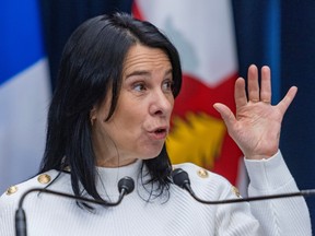 Montreal mayor valerie plante is seeing gesturing with a hand up in front of a flag, standing at a podium.