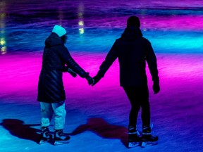 Two people are seen from behind, wearing black, skating down a rink bathed in pink and blue lights.