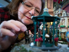 A woman carefully places miniature pieces under a miniature gazebo.