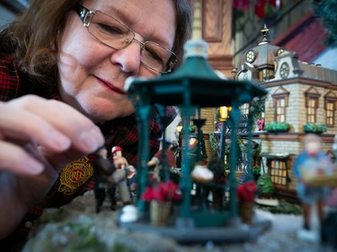 A woman places people in a miniature Christmas village.