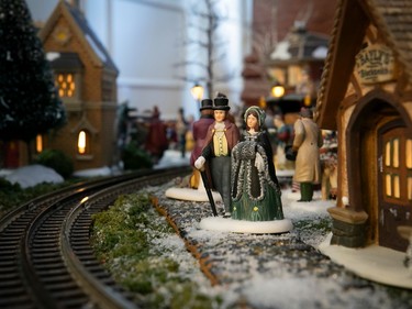 Two tiny people stand by train tracks in a miniature Christmas village.