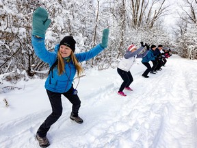 A handful of people are doing cario exercises in the snow, on a path lined with trees.