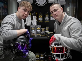 Brothers Liam, left, and Dylan Burger are seen with some of the equipment made by the company they founded called Nxtrnd, including two helmets they are resting their arms on, gloves and mouthguards seen behind them.