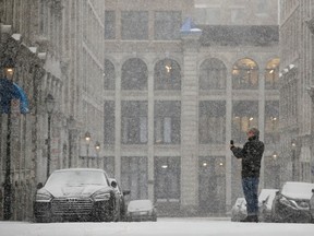 A Montreal street covered in snow, with a building in the background. A man to the right of the frame is taking a photo with a phone.