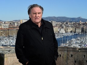 Gérard Depardieu stands outside with a cityscape in the background