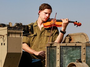 An Israeli soldier playing violin on a tank.
