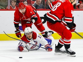 Brendan Gallagher looks at the puck while lying on the ice under a crouching Hurricanes player