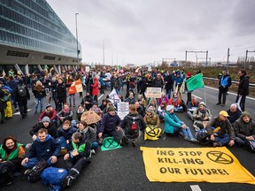 Protesters sit by a banner reading "ING Stop Kill-ING Our Future!" during a blockade action of the A10 highway by enviromentalist group Extinction Rebellion in front of the former headquarters of Dutch multinational banking and finance corporation, ING to protest against the bank's financing services to the fossil industry, in Amsterdam on Saturday, Dec. 30, 2023.