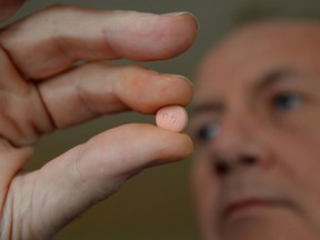 Photo shows close-up of fingers holding a tablet of an anti-cholesterol drug.