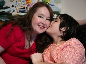 A woman smiles at the camera as her daughter kisses her cheek.