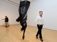 A man stands beside a museum exhibit that is the statue of liberty, but black, suspended upside down.