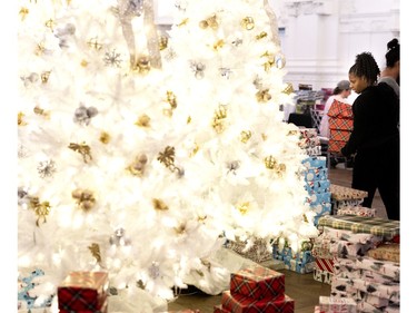 Andrienne Bowra, a schoolteacher who volunteered to wrap gifts, looks for space under the tree during the Montreal Community Cares Christmas Gift Wrapping Party, in Montreal, on Sunday, Dec. 3, 2023.