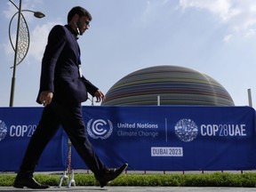 A person walks by a sign for the COP28 UN Climate Summit, Wednesday, Nov. 29, 2023, in Dubai, United Arab Emirates.