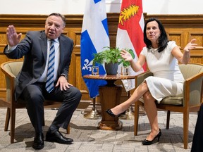 François Legault and Valérie Plante gesture while sitting at a small table in front of Quebec and Montreal flags