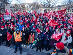 Hundreds of people carrying red FAE flags stand on a street outside McGill University's Roddick Gates
