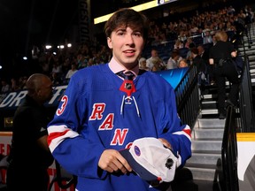 Drew Fortescue wears a Rangers jersey and carries a cap in his hand in the stands of an arena
