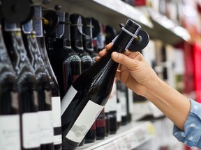 A hand pulls a bottle of wine off a grocery store shelf