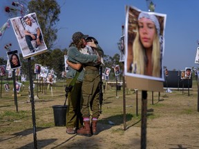 Israeli soldiers embrace next to photos of people killed and taken captive by Hamas militants during their violent rampage through the Nova music festival in southern Israel, which are displayed at the site of the event, to commemorate the Oct. 7, massacre, near kibbutz Re'im, Friday, Dec. 1, 2023.