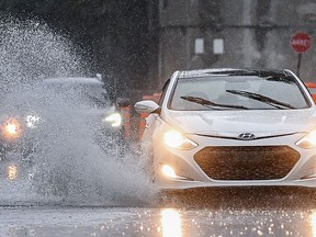 A motorist makes their way along a street through pooling water during heavy rain in Montreal, Saturday, Oct. 7, 2023.