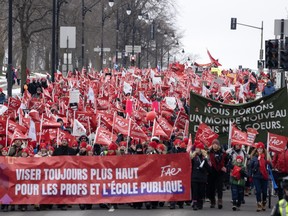 Striking teachers wave red flags as they march down a wide street