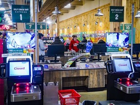 Customers check out at registers with cashiers near a section of self-checkout kiosks.