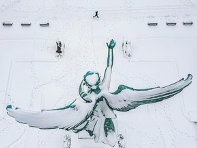 A statue is seen from above, covered in snow, with a person jogging near it.