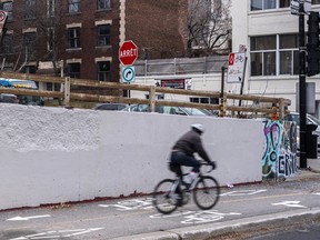 A cycling rides on a bike path past a cement retaining wall