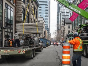A crane removes construction material from a large flatbed truck parked on a downtown street