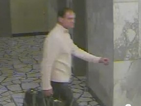 A blurry security camera still shows a man in a white sweater carrying a bag in a hallway