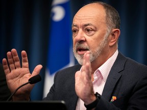 A man gestures during a press conference. There is a Quebec flag behind him.