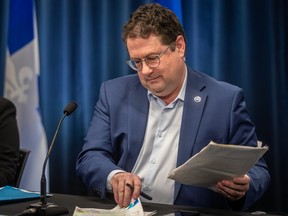 Bernard Drainville handles papers while seated at a table in front of a microphone