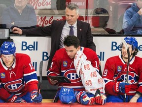 Canadiens captain Nick Suzuki consults a tablet on the bench in front of head coach Martin St-Louis during game last week against San Jose at the Bell Centre. Suzuki was flanked on the bench by Mitchell Stephens, left, and Raphael Harvey-Pinard.