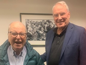 Peter Pearson and Ken Dryden smiling in front of a photo of hockey players.