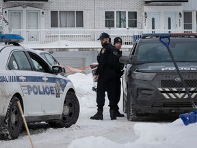 Two officers stand between police vehicles in a residential neighbourhood.