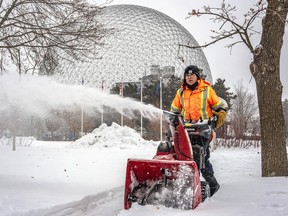 A man pushes a snowblower with the Biosphere in the background.