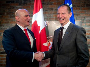 Federal Employment Minister Randy Boissonnault and Quebec Finance Minister Eric Girard shake hands in front of the Canadian and Quebec flags.