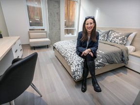 A woman sits on a bed in a room decorated in grey and white.