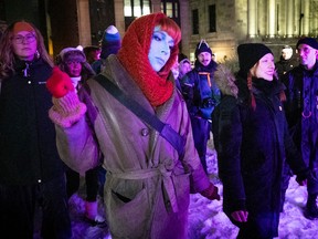 A woman in a red scarf and blue face makeup is part of a protest on a winter street.