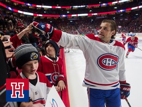 A hockey player hands a puck to a kid with outstretched arms in the stands