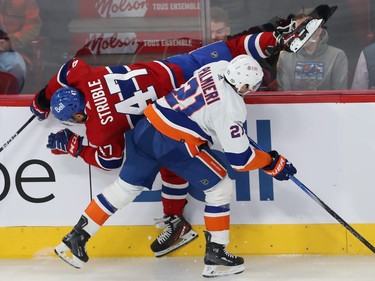 Montreal Canadiens' Jayden Struble is splayed horizontally along the boards next to New York Islanders' Kyle Palmieri