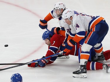 Montreal Canadiens' Josh Anderson falls to the ice between two Islanders players, all three looking at the puck in front of them