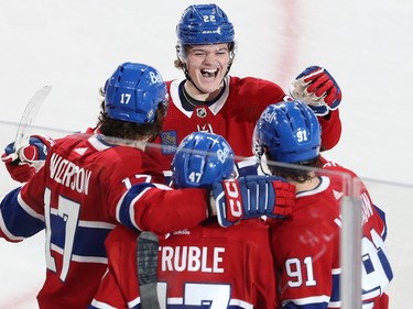 Canadiens' Cole Caufield smiles as he skates to embrace three teammates on the ice
