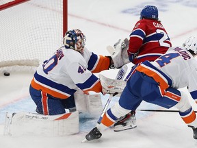 The puck is in the back of the Islanders net behind the goaltender and another Islanders player as Canadiens' Cole Caufield follows through on a shot