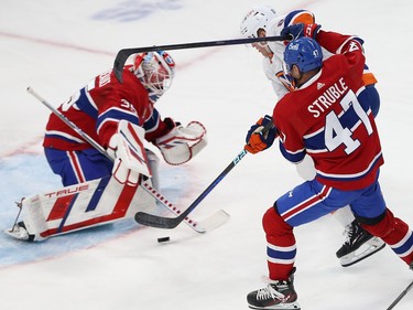 The puck sits just outside the crease between New York Islanders' Hudson Fasching and Canadiens goaltender Sam Montembeault with Canadiens' Jayden Struble right behind Fasching