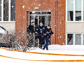 Three police officers leave an apartment complex. It is snowing and there is crime-scene tape in the foreground.