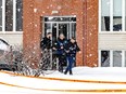 Three police officers leave an apartment complex. It is snowing and there is crime-scene tape in the foreground.