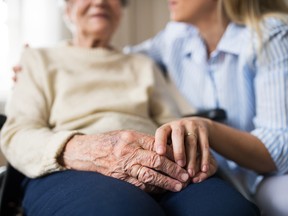 A woman holds the hand of an elderly person.