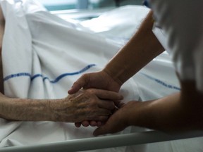 A nurse holds the hand of an elderly patient in a palliative care unit.