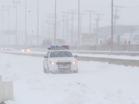 A police car is seen through the snow driving down a highway